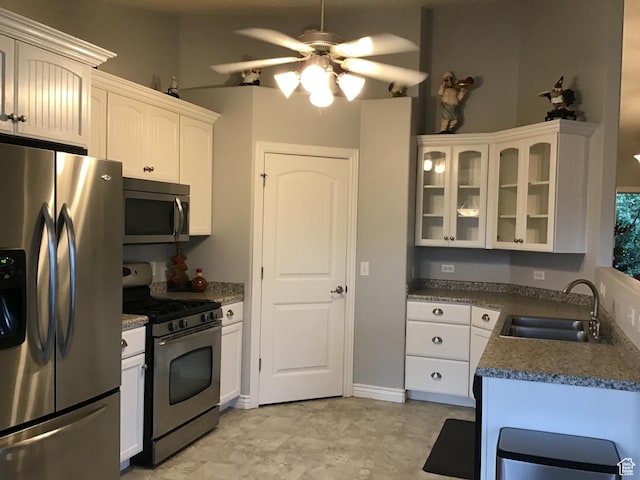kitchen with white cabinets, dark countertops, glass insert cabinets, appliances with stainless steel finishes, and a sink