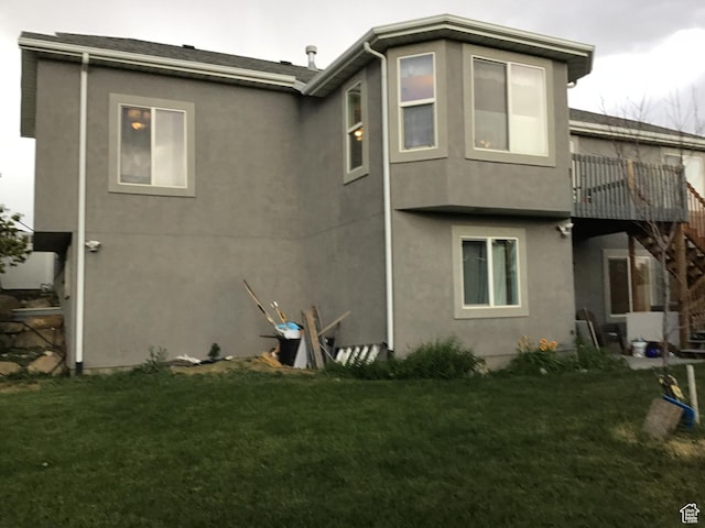 back of property with a lawn, stairway, and stucco siding