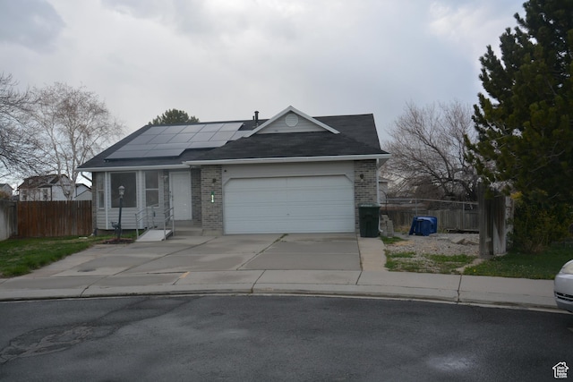 ranch-style home with driveway, fence, brick siding, roof mounted solar panels, and a garage