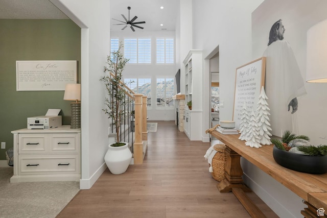 corridor featuring recessed lighting, light wood finished floors, a towering ceiling, and baseboards