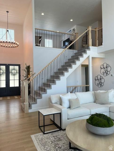 living area with a notable chandelier, wood finished floors, a towering ceiling, french doors, and stairs