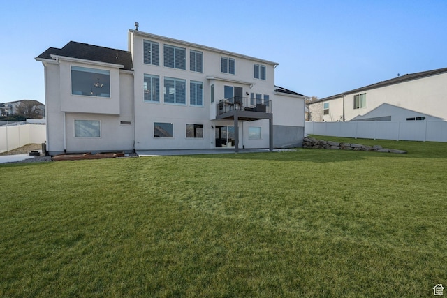 rear view of property featuring a yard, stucco siding, fence, and a balcony