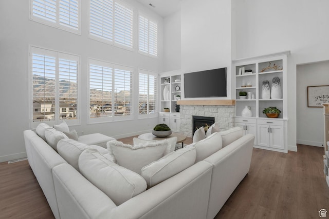 living room with a stone fireplace, a high ceiling, and wood finished floors