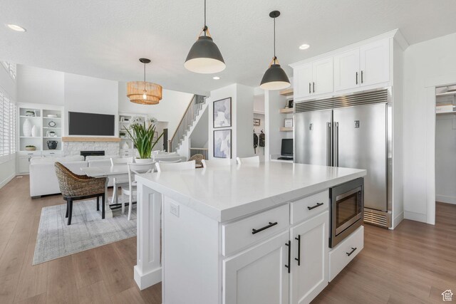 kitchen with built in appliances, light countertops, white cabinetry, decorative light fixtures, and wood finished floors