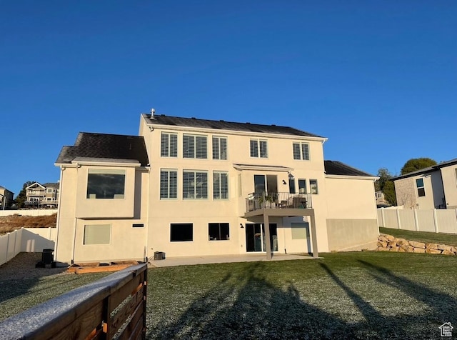 back of property with a yard, stucco siding, fence, and a balcony