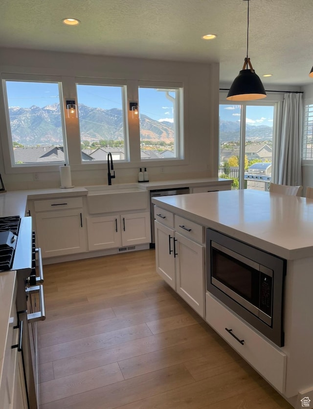 kitchen with stainless steel microwave, light wood-type flooring, light countertops, white cabinets, and a sink