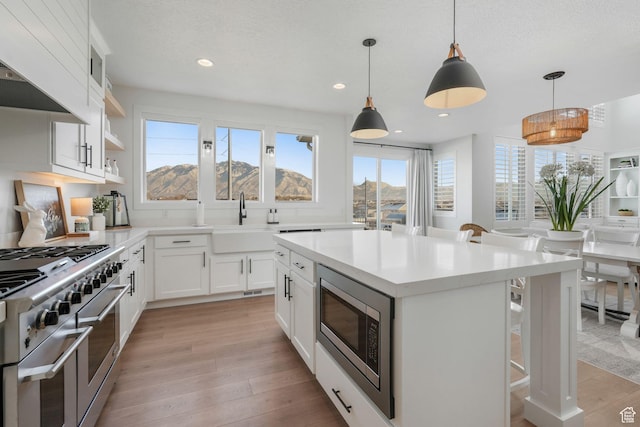 kitchen with a sink, light wood-type flooring, appliances with stainless steel finishes, a breakfast bar, and pendant lighting