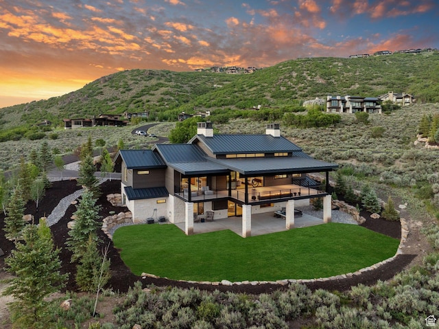 back of house with a chimney, metal roof, a standing seam roof, a patio area, and a mountain view