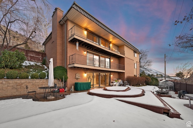 3604 S Crestwood Dr, Salt Lake City, UT 84109 - snow covered back of property featuring a balcony, brick siding, fence, a chimney, and a patio area