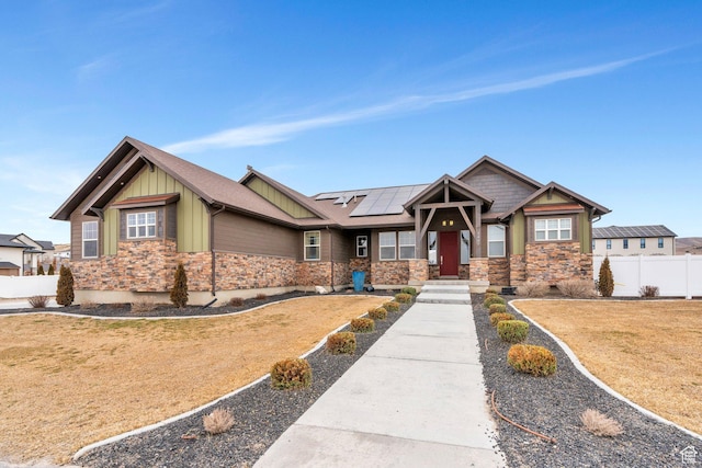 craftsman-style home featuring solar panels, fence, stone siding, a front lawn, and board and batten siding