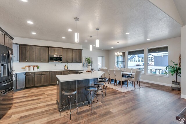 1407 E Abigail Ln, Eagle Mountain, UT 84005 - kitchen with light countertops, stainless steel microwave, black refrigerator with ice dispenser, light wood-style floors, and dark brown cabinets