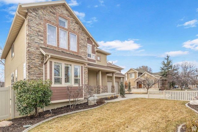 rear view of property featuring stone siding, a yard, concrete driveway, and fence