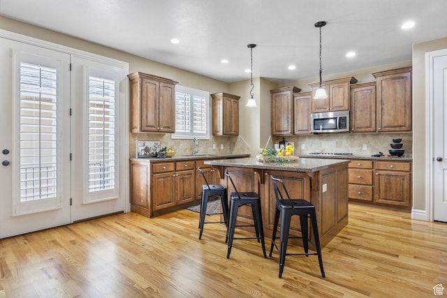 kitchen featuring a kitchen breakfast bar, brown cabinetry, a center island, light wood finished floors, and stainless steel microwave