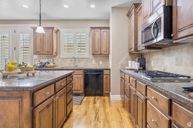 kitchen featuring stainless steel appliances, brown cabinetry, dark stone counters, a sink, and light wood-type flooring