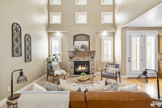 living area featuring visible vents, a towering ceiling, a stone fireplace, wood finished floors, and baseboards