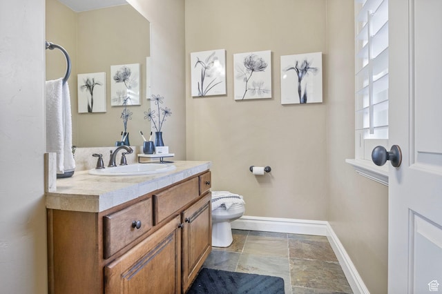 bathroom featuring stone finish floor, toilet, vanity, and baseboards