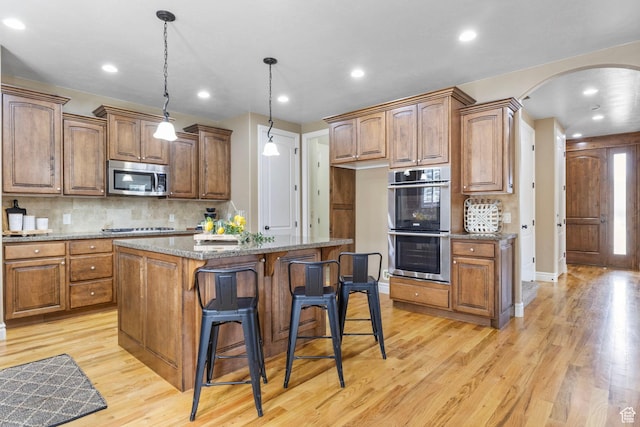 kitchen featuring arched walkways, decorative backsplash, a center island, stainless steel appliances, and light wood-type flooring