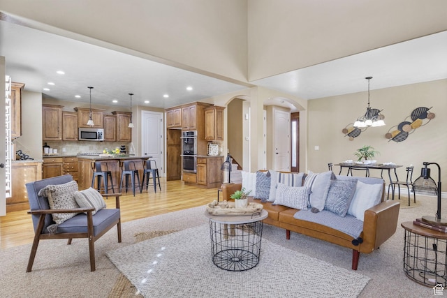 living area with light wood-style floors, arched walkways, a chandelier, and recessed lighting