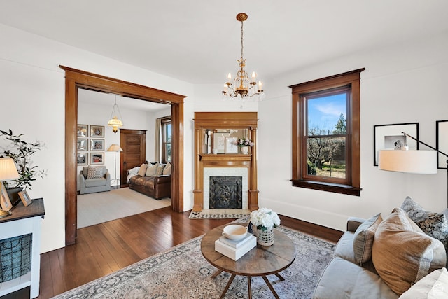 living room with dark wood-type flooring, an inviting chandelier, baseboards, and a brick fireplace