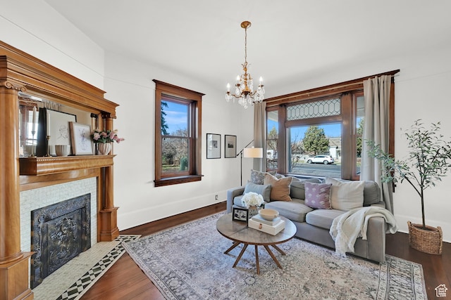 living room with a tile fireplace, dark wood-type flooring, a notable chandelier, and baseboards