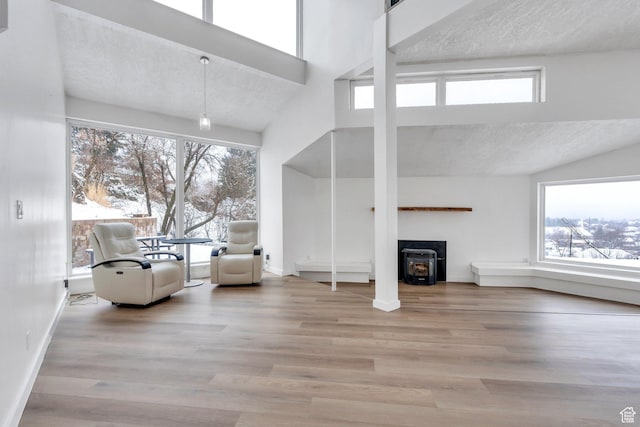 unfurnished living room featuring a wood stove, plenty of natural light, a textured ceiling, and wood finished floors