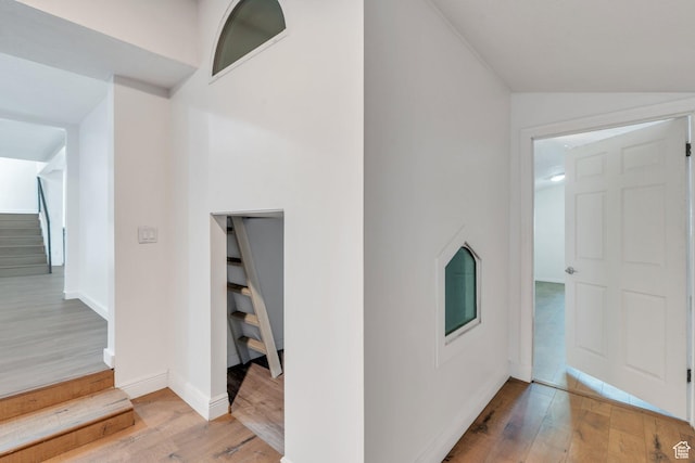 corridor featuring stairs, vaulted ceiling, wood finished floors, and baseboards