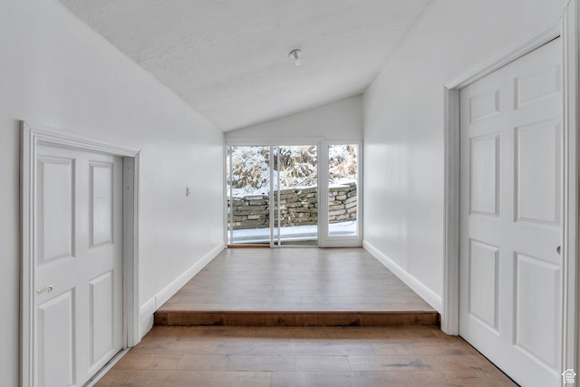 interior space with a textured ceiling, baseboards, vaulted ceiling, and hardwood / wood-style floors
