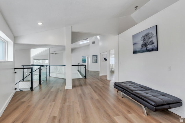 corridor with light wood-style floors, baseboards, vaulted ceiling, and an upstairs landing