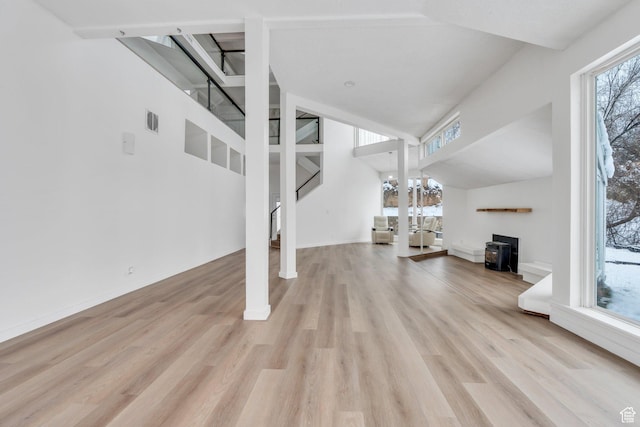 unfurnished living room featuring visible vents, a wood stove, high vaulted ceiling, light wood-type flooring, and stairs