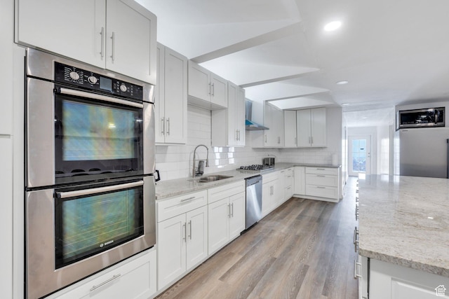 kitchen with decorative backsplash, light stone counters, stainless steel appliances, wall chimney range hood, and a sink