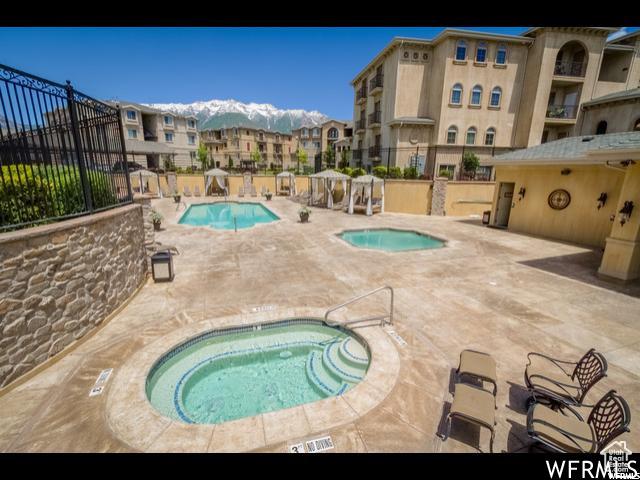 community pool with fence, a patio area, a mountain view, and a hot tub