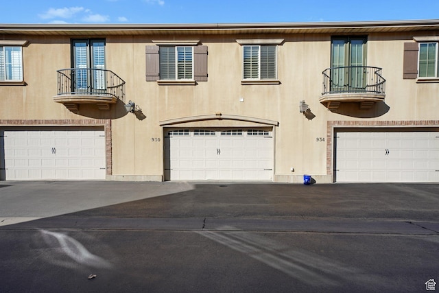 townhome / multi-family property with aphalt driveway, a balcony, and an attached garage