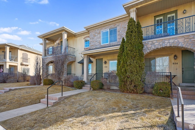 view of front facade featuring covered porch, stucco siding, a balcony, and stone siding