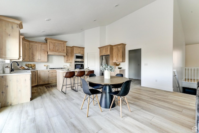 dining area with high vaulted ceiling, baseboards, and light wood-style floors