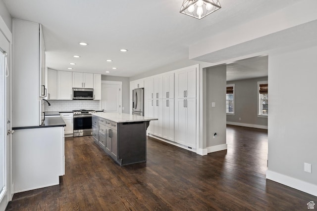 kitchen with stainless steel appliances, dark wood-type flooring, a kitchen island, white cabinets, and decorative backsplash