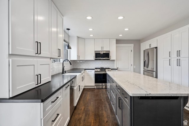 kitchen featuring stainless steel appliances, a sink, white cabinetry, decorative backsplash, and a center island