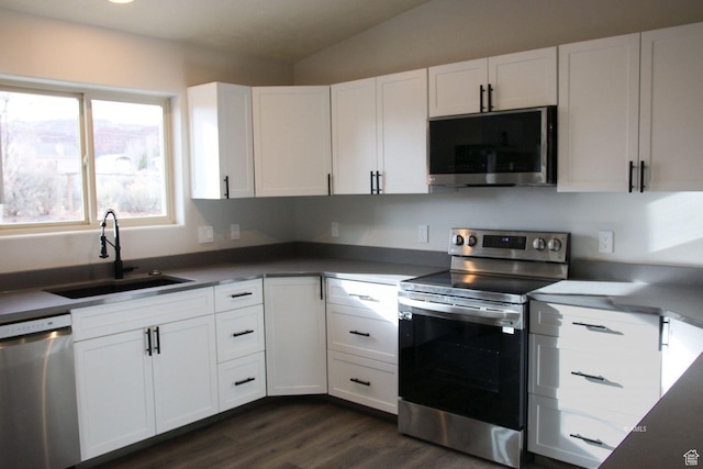 kitchen with appliances with stainless steel finishes, dark wood-type flooring, vaulted ceiling, white cabinetry, and a sink