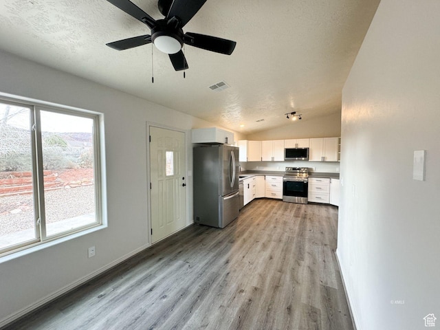 kitchen featuring white cabinets, lofted ceiling, stainless steel appliances, a textured ceiling, and light wood-style floors