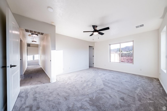 carpeted empty room with a ceiling fan, visible vents, and baseboards
