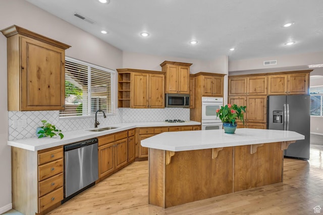 kitchen featuring light wood finished floors, stainless steel appliances, visible vents, a sink, and a kitchen island