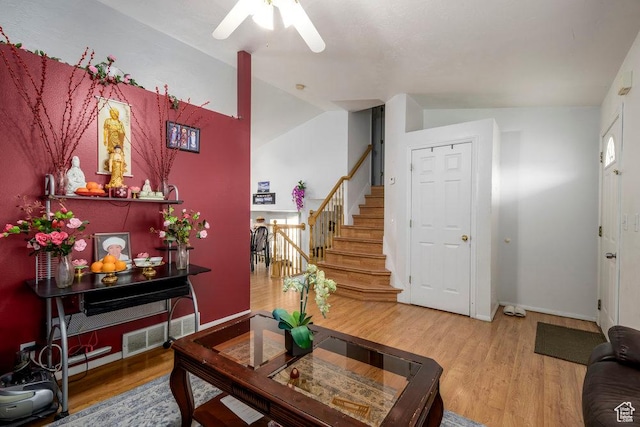 living room featuring wood finished floors, visible vents, a ceiling fan, vaulted ceiling, and stairs