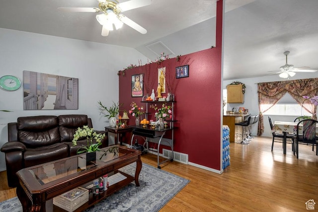living room featuring attic access, visible vents, lofted ceiling, light wood-style flooring, and ceiling fan
