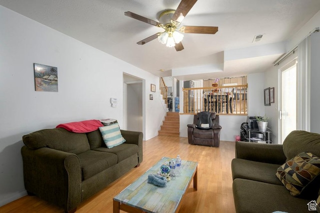 living area featuring a ceiling fan, stairway, visible vents, and light wood-style floors