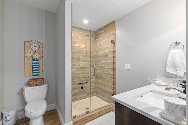 bathroom with a stall shower, toilet, a sink, a textured ceiling, and baseboards