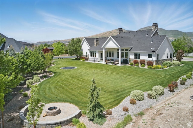 back of property with an outdoor fire pit, a patio area, a yard, and a chimney