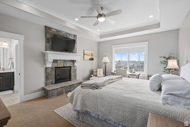 bedroom featuring light colored carpet, a stone fireplace, a tray ceiling, recessed lighting, and baseboards