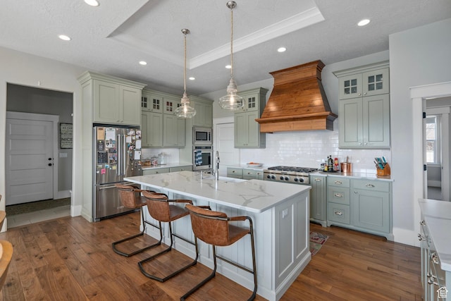 kitchen with stainless steel appliances, custom range hood, a tray ceiling, a sink, and backsplash