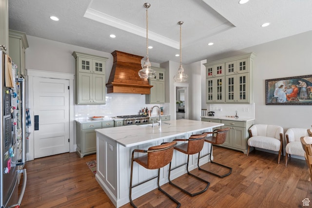 kitchen with custom range hood, a tray ceiling, a sink, tasteful backsplash, and dark wood-style flooring