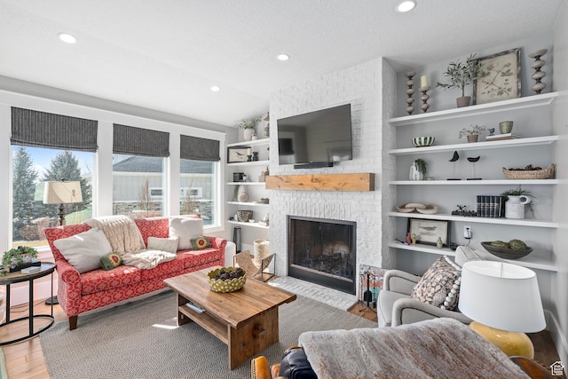living area with wood finished floors, a textured ceiling, a brick fireplace, recessed lighting, and vaulted ceiling