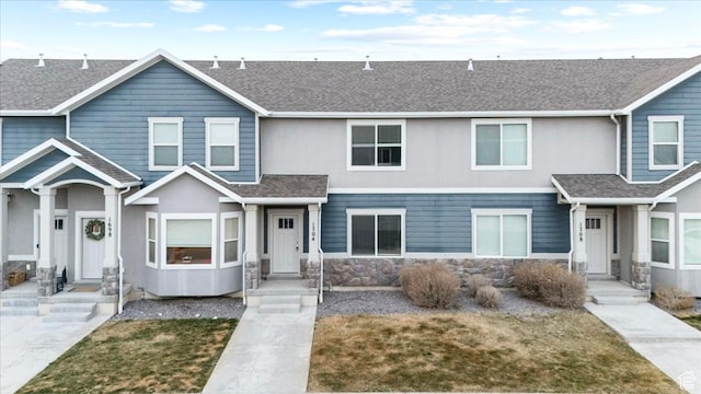 multi unit property with stone siding, roof with shingles, and stucco siding